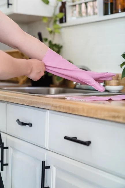 A close-up view of a hand wiping down a stovetop with a spray bottle and cloth.