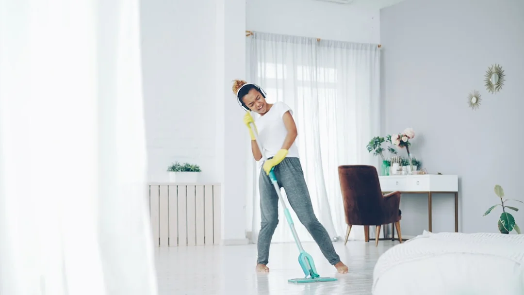 A cleaner wearing protective coveralls and gloves is vacuuming a contemporary living room.